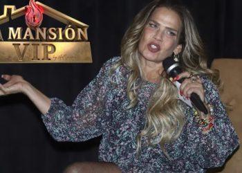 Female presenter on a dark stage, speaking into a handheld microphone, wearing a floral dress with bracelets; 'La Mansión VIP' logo appears in the upper left.