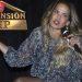 Niurka-bobby-mansion-vip › Guadalupa Ciudadana Female Presenter on a Dark Stage, Speaking into a Handheld Microphone, Wearing a Floral Dress with Bracelets; 'la Mansión Vip' Logo Appears in the Upper Left. › Guadalupa Ciudadana