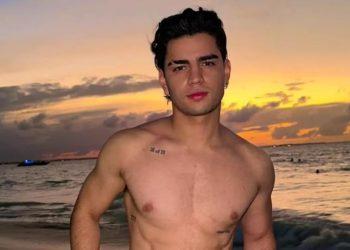 Aaron-mercury-tendencias › Guadalupa Ciudadana Shirtless Young Man Posing on a Sandy Beach at Sunset, with Tattooed Chest and Calm Ocean in the Background › Guadalupa Ciudadana