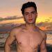 Shirtless Young Man Posing on a Sandy Beach at Sunset, with Tattooed Chest and Calm Ocean in the Background › Guadalupa Ciudadana