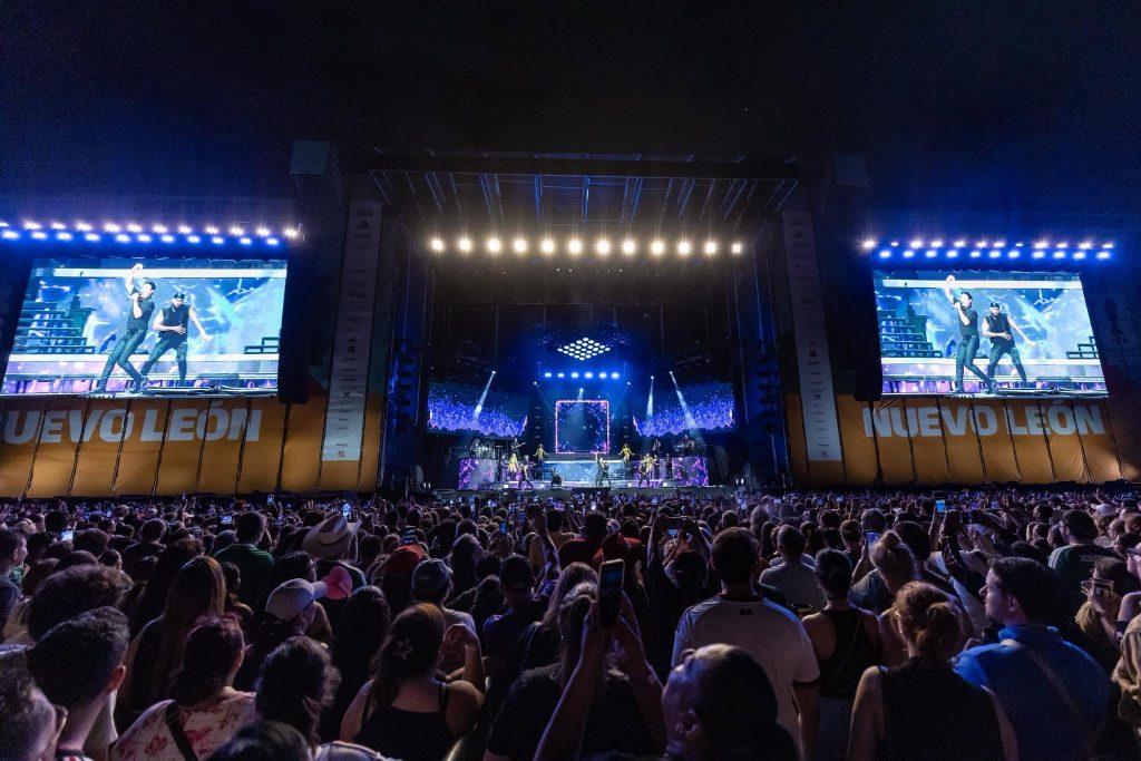 Outdoor Nighttime Concert with a Large Crowd and a Brightly Lit Stage, Two Side Screens Showing Performers, and Blue Stage Lighting. › Guadalupa Ciudadana
