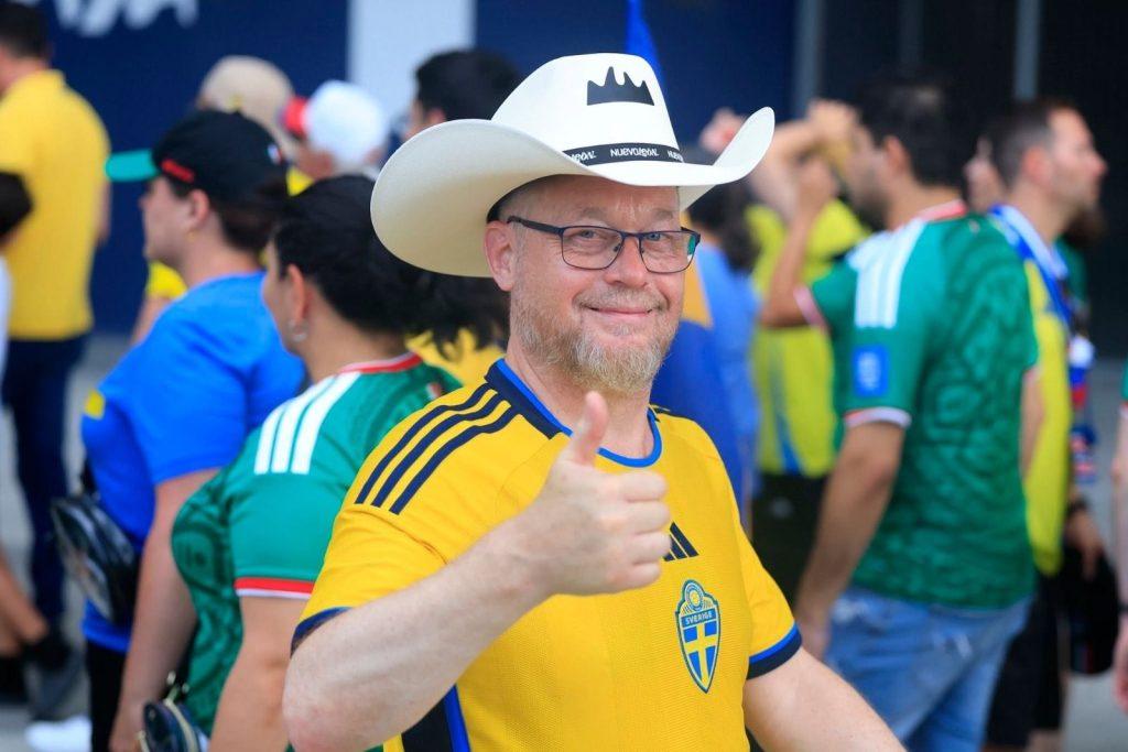 Smiling Man in a Yellow Sweden Soccer Jersey, Wearing a White Cowboy Hat, Giving a Thumbs Up Among a Crowd of Fans. › Guadalupa Ciudadana