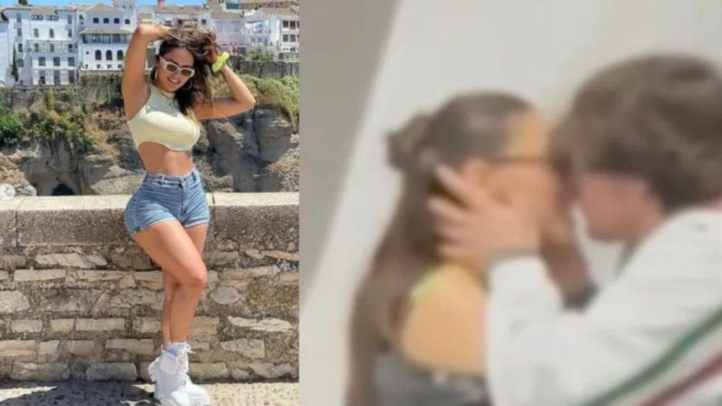 Young Woman Posing Outdoors in a Pale Yellow Crop Top and Denim Shorts, Leaning on a Stone Wall with a Coastal Town Behind Her. › Guadalupa Ciudadana
