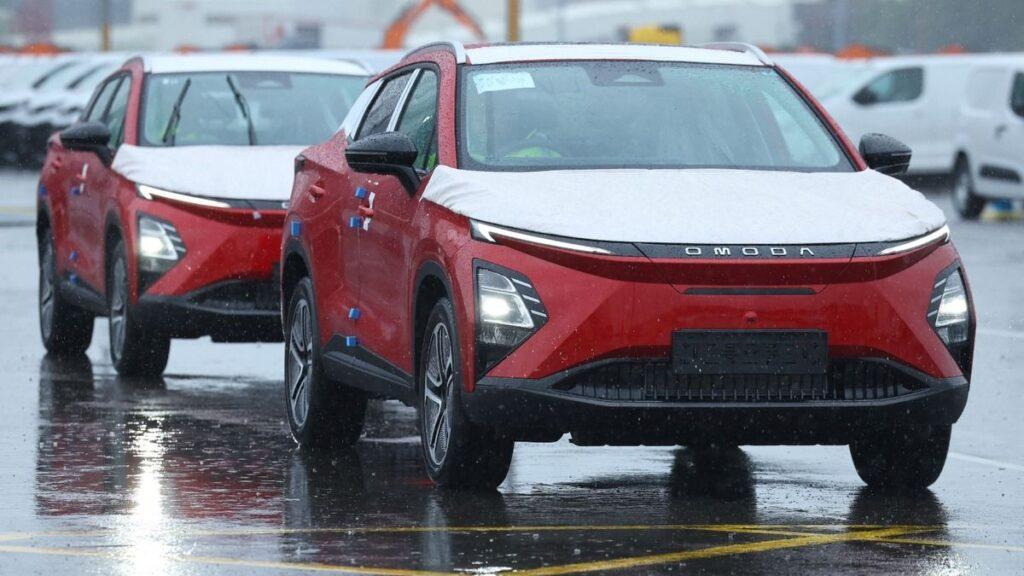 Fabricacion-de-autos-chinos-mexico › Guadalupa Ciudadana Red Omoda Electric Suv in a Rainy, Snow-dusted Car Lot, Line of Vehicles Ahead and Reflections on Wet Pavement. › Guadalupa Ciudadana
